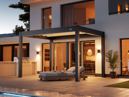  A sleek, modern, dark gray pergola with integrated LED strip lighting provides shade over a patio area next to a contemporary white house. Beneath the pergola is a comfortable-looking gray outdoor chaise lounge. The house features large glass doors and windows that showcase warm, inviting interior lighting. On the patio, there are also a built-in outdoor grill area and a potted plant. The overall atmosphere is luxurious and serene, illuminated by the soft interior and accent lighting at dusk