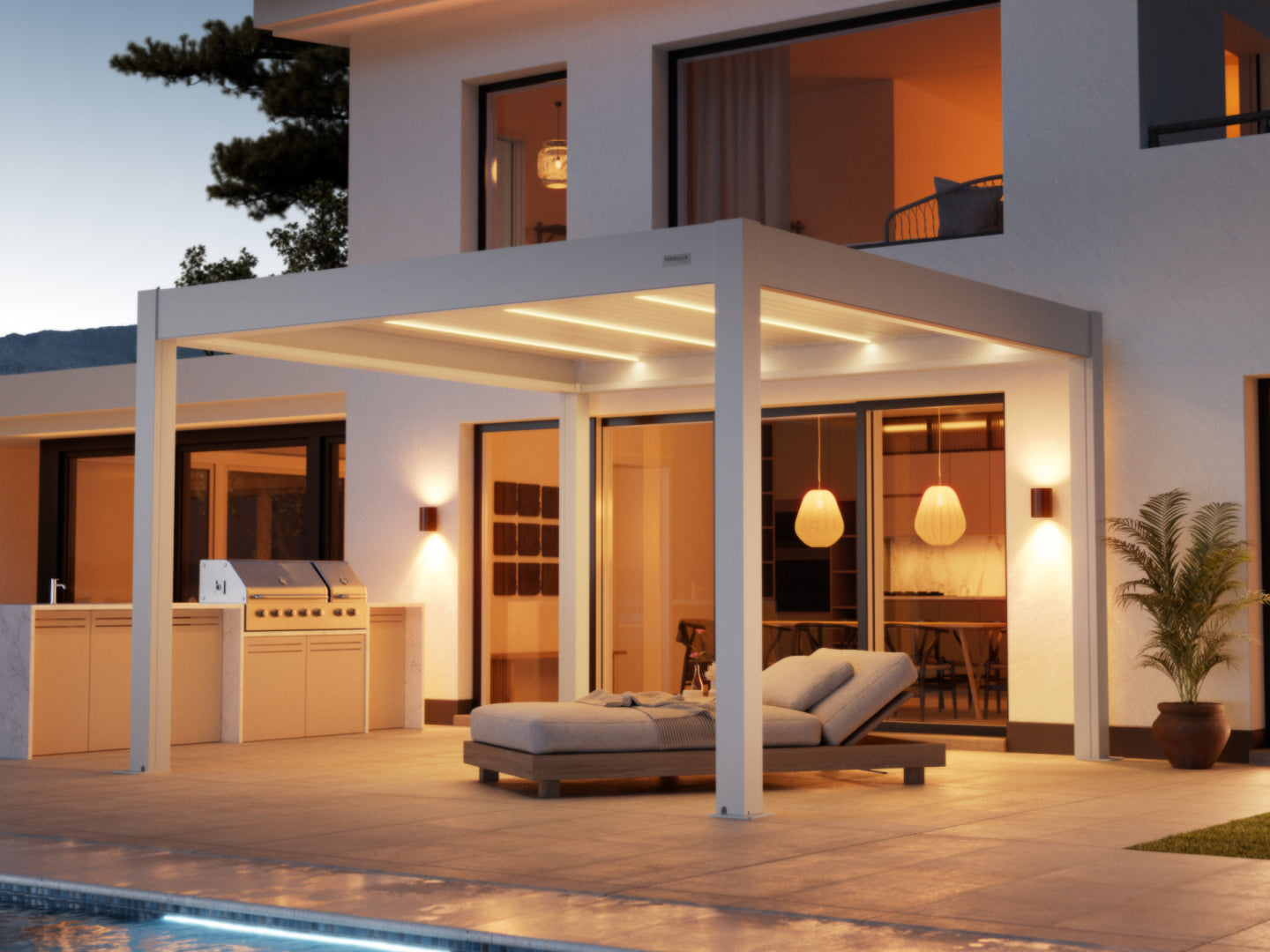  A contemporary white pergola with integrated LED strip lighting provides shade over a paved patio area next to a modern white stucco house at dusk. Underneath the pergola, a comfortable-looking chaise lounge with gray cushions is positioned for relaxation. The patio also features a built-in outdoor kitchen and grill on the left and a potted plant on the right. Large glass doors and windows reveal a warm, inviting interior with pendant lighting. A swimming pool's edge is visible in the foreground.