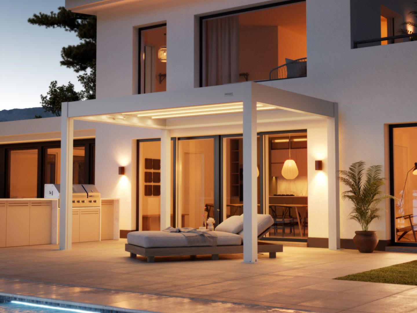  A contemporary white pergola with integrated LED strip lighting provides shade over a paved patio area next to a modern white stucco house at dusk. Underneath the pergola, a comfortable-looking chaise lounge with gray cushions is positioned for relaxation. The patio also features a built-in outdoor kitchen and grill on the left and a potted plant on the right. Large glass doors and windows reveal a warm, inviting interior with pendant lighting. A swimming pool's edge is visible in the foreground.